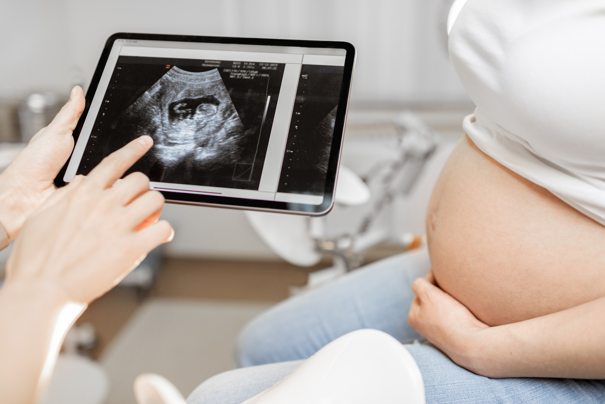 Schwangerschaft und klinische Studien | Novartis - klinsiche Forschung - Arzt zeigt schwangeren Frau Ultraschallbild auf Tablet