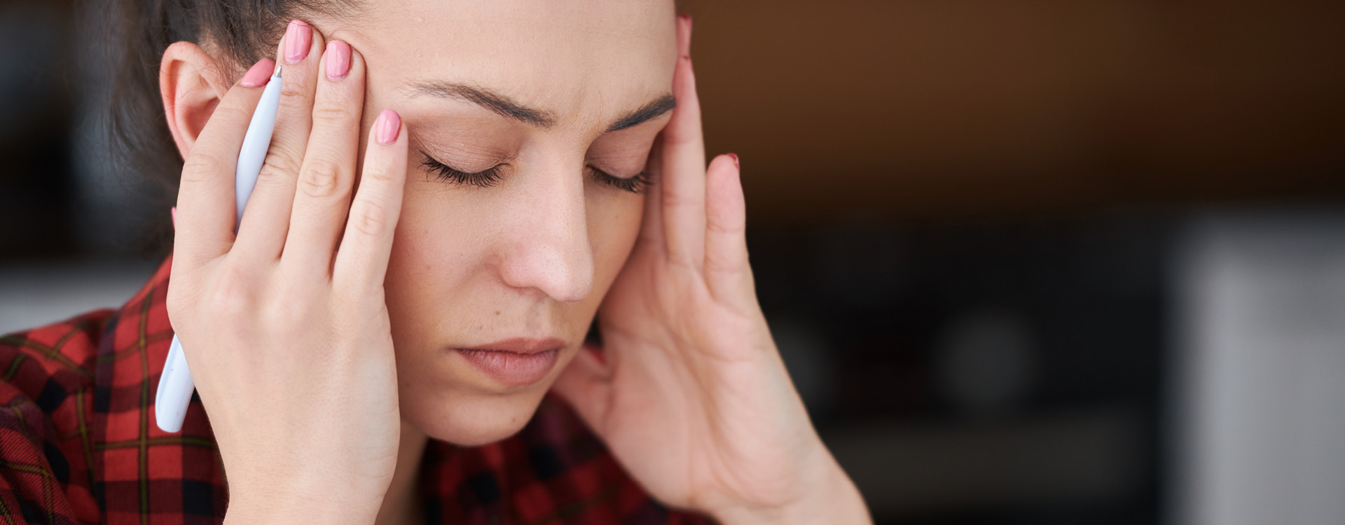 novartis-klinische-forschung-gut-informiert-gesundheitswissen-migraene-prophylaxe Eine junge Frau reibt sich die Schläfen aufgrund von Kopfschmerzen vor neutralem, dunklen Hintergrund.