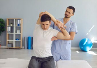 Chiropractor or physiotherapist examining young man's arm to help him cure health problems Physiotherapeut dehnt den Arm seines Patienten | Novartis – Klinische Forschung