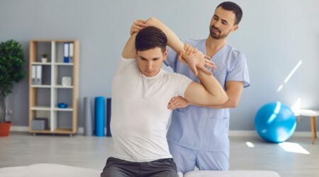 Chiropractor or physiotherapist examining young man's arm to help him cure health problems Physiotherapeut dehnt den Arm seines Patienten | Novartis – Klinische Forschung