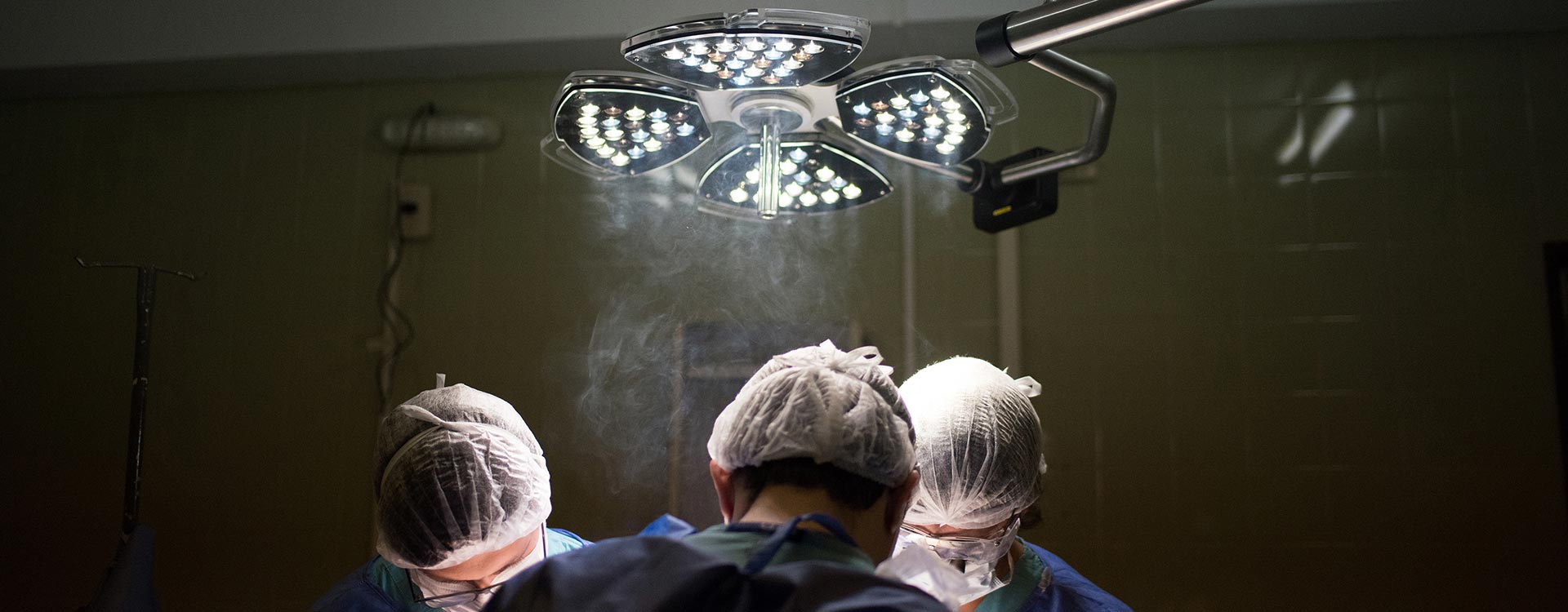 Drei Ärzte stehen im OP unter einer Lampe | Härtefallprogramm | Novartis – Klinische Forschung