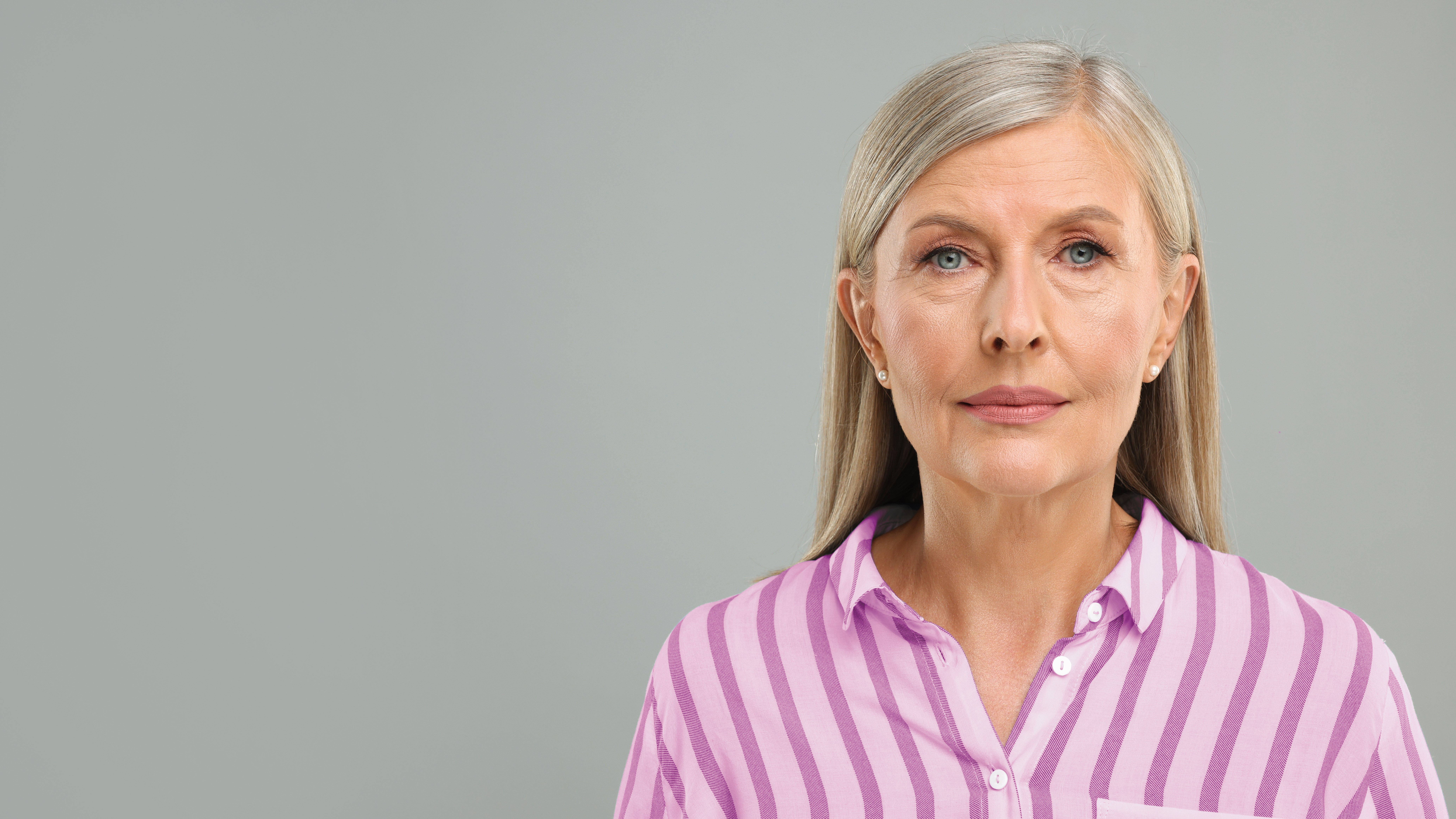 Ältere Frau mit langem grauem Haar vor grauem, neutralem Hintergrund.