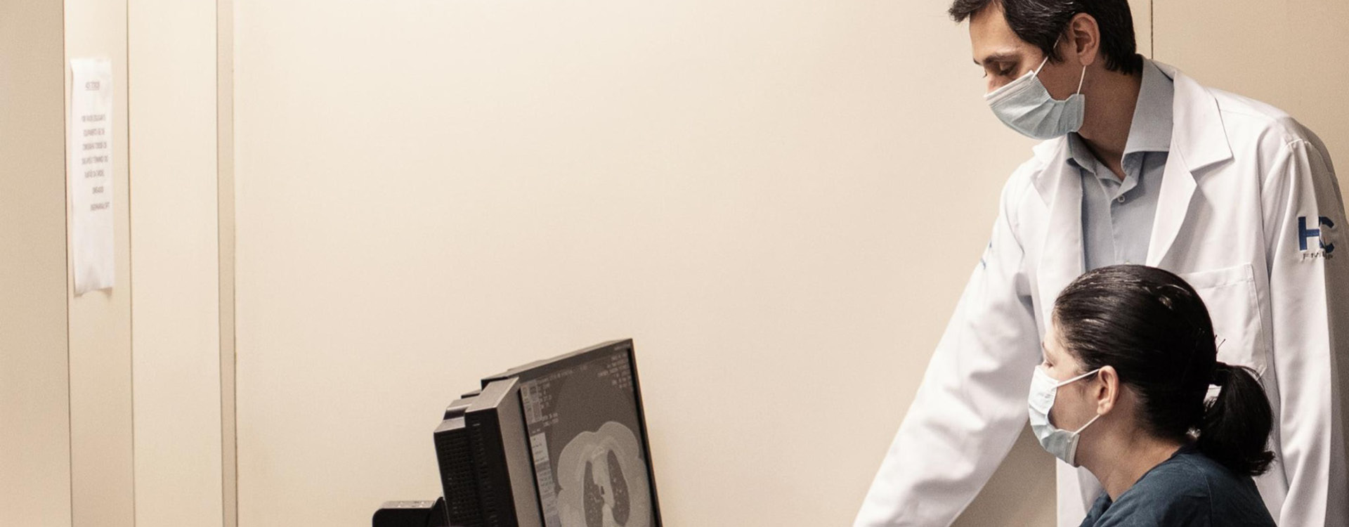 novartis-klinische-forschung-gut-informiert-gesundheitswissen-radioligandentherapie Ein Arzt und medizinische Fachkraft mit Mundschutz betrachten gemeinsam eine Röntgenaufnahme auf einem Monitor.