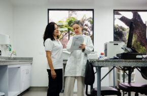 Eine weibliche medizinische Fachkraft zeigt einer Frau Ergebnisse auf einem Ausdruck in einem Behandlungszimmer.