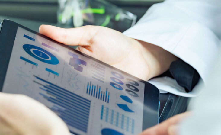 Hände einer Person in Laborkleidung, die ein Tablett halten, auf dem eine Grafik mit Daten angezeigt wird