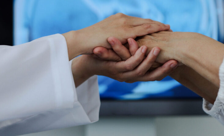 Die Hand einer Person in weißer Kleidung hält die Hand eines Patienten