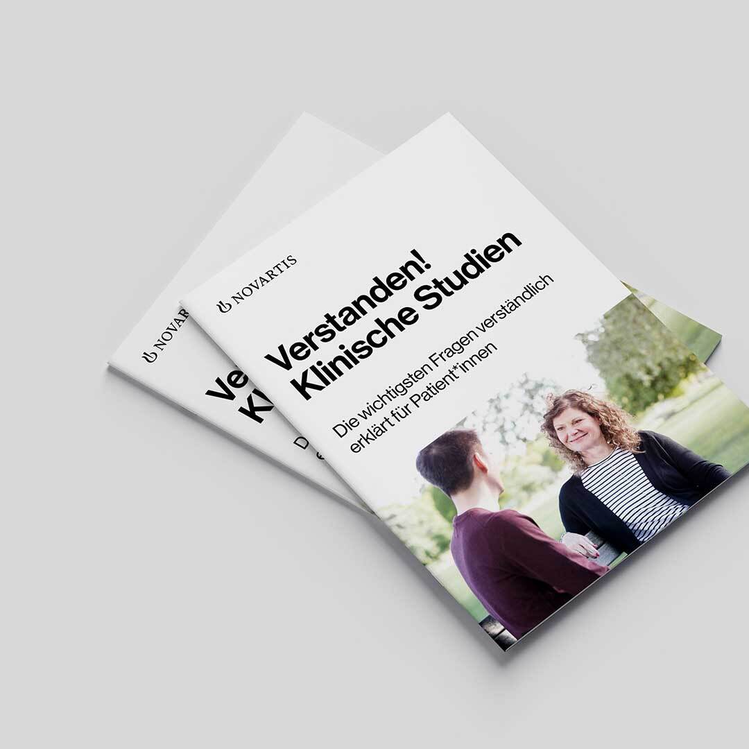 Zwei Exemplare der "Verstanden! Klinische Studien"-Broschüre auf blauem Hintergrund.