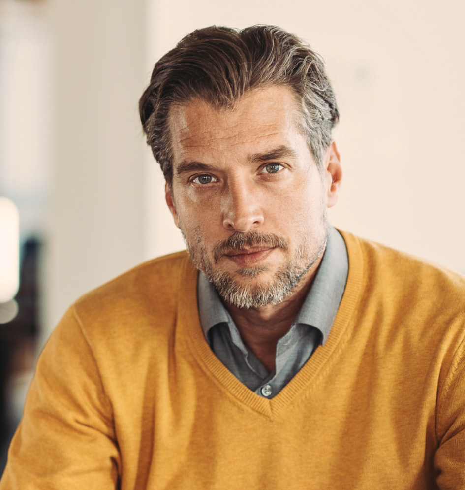 Mann mit orangefarbenem Pullover blickt in Kamera