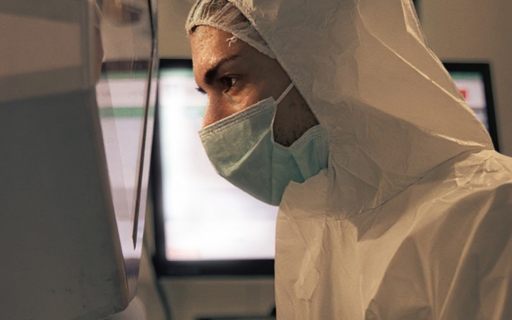 Eine Person in Schutzkleidung und Mundschutz arbeitet an einem Laborgerät.