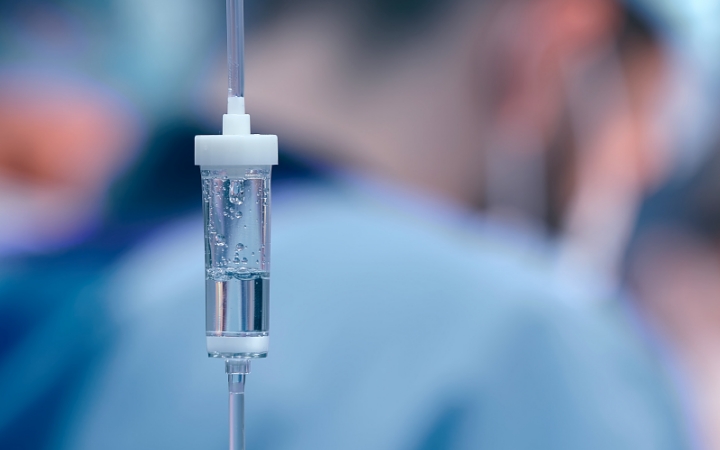 Infusionsbeutel mit Tropfkammer vor unscharfem Hintergrund in einer Klinik.