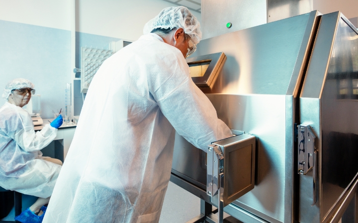 Zwei Mitarbeitende in Schutzkleidung arbeiten an Laborgeräten in einem Reinraum.