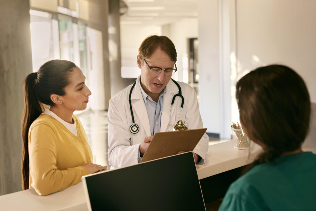Ein Arzt erläutert einer Patientin medizinische Unterlagen an einem Empfangstresen.