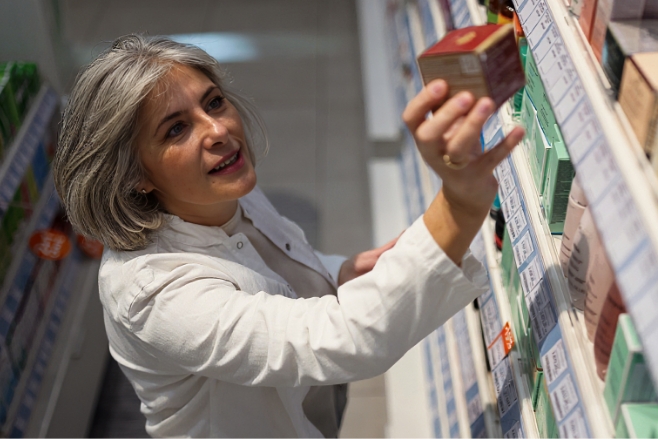Frau in weißem Kittel nimmt eine Schachtel aus dem Regal